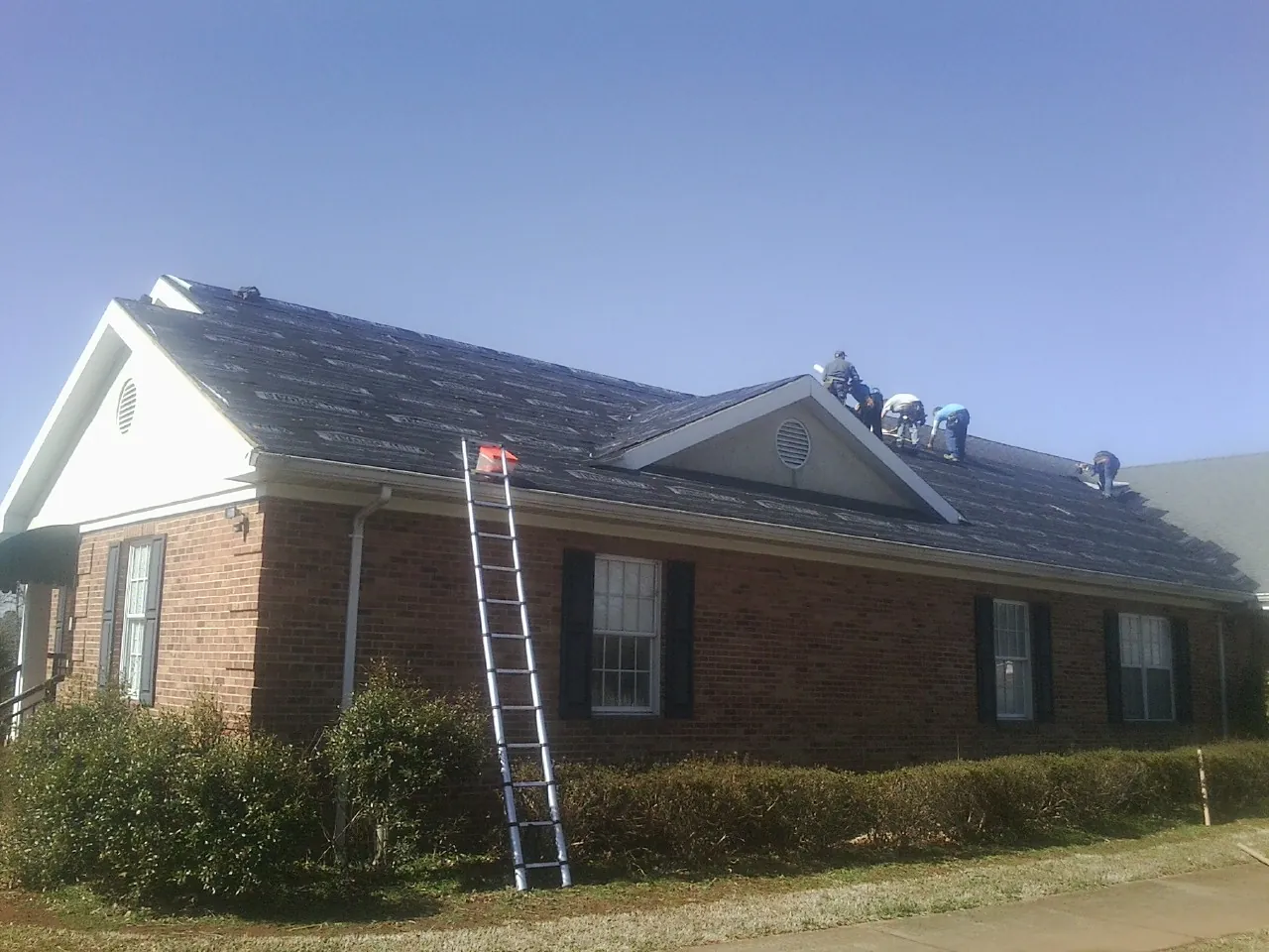 Crew tearing shingles off a brick ranch roof with a ladder set — Metal Roof Repair work by our crew in Shelbyville
