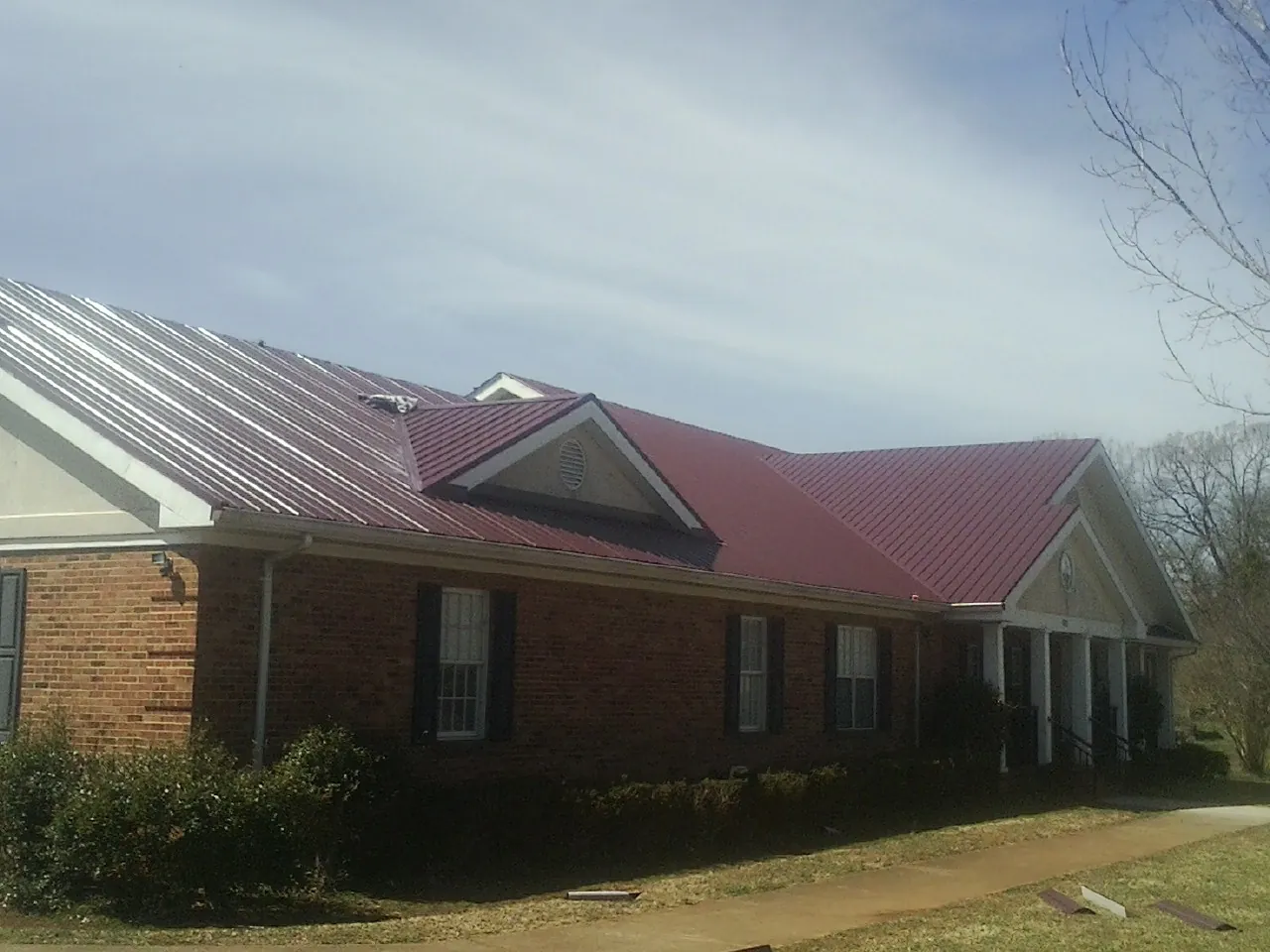 Red metal roof with gabled entries on a long brick building, from a Hail Damage Roof Repair job in Shelbyville