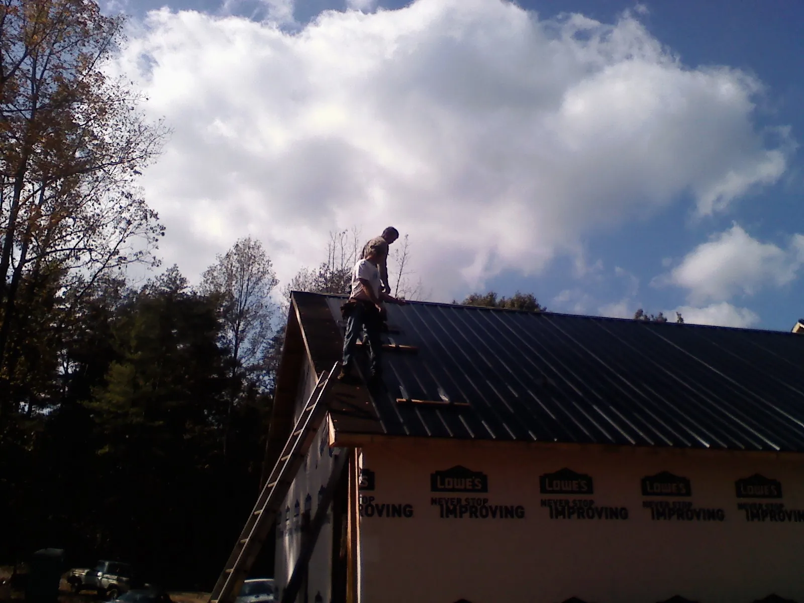 Roofer fastening dark metal panels high against a cloudy sky, from a Roof Inspection job in Shelbyville