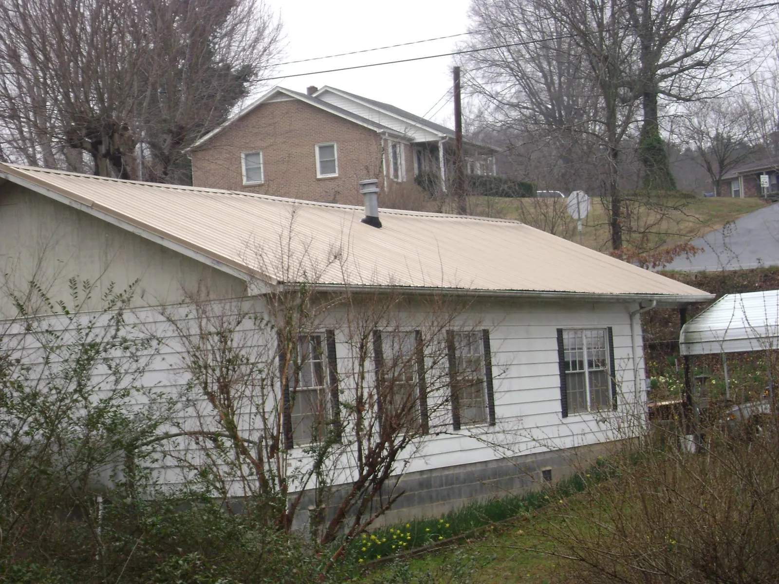 Tan metal roof on a white sided house set into a hillside — Commercial Roofing by Roofing Brothers in Shelbyville